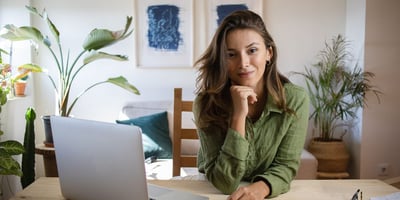 A woman is considering the pros and cons of remote working at her table at home to do telework on her laptop.